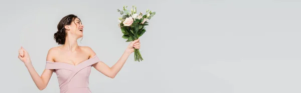 Fiancée excitée montrant geste de victoire tout en tenant le bouquet de mariage isolé sur gris, bannière — Photo de stock