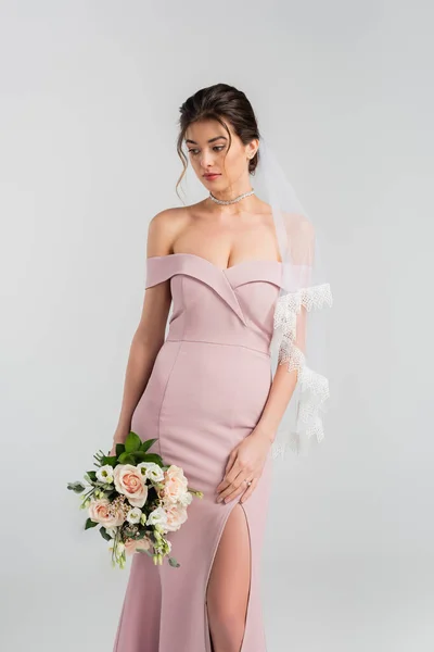 Giovane sposa in abito rosa e velo con bouquet da sposa isolato su grigio — Foto stock