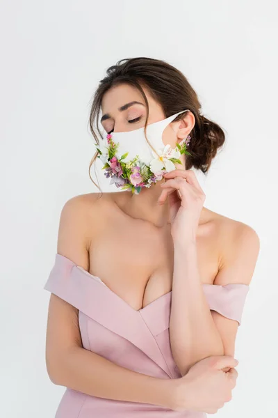 Frau in rosa Kleid und medizinischer Maske mit Blumen posiert isoliert auf grau — Stockfoto