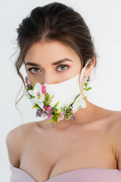 Brünette Frau in medizinischer Maske mit Blumen, die isoliert auf grau in die Kamera schauen — Stockfoto