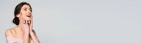 Excited bride looking away while touching face isolated on grey, banner — Stock Photo