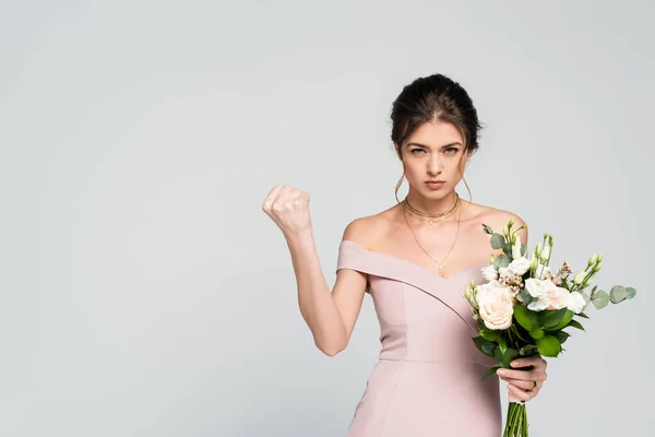 Femme sérieuse montrant poing serré tout en tenant le bouquet de mariage isolé sur gris — Photo de stock