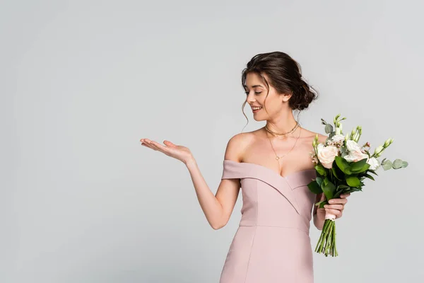 Donna allegra che punta con mano mentre in piedi con bouquet di nozze isolato su grigio — Foto stock