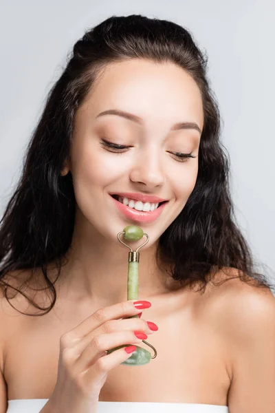 Happy woman using jade roller while massaging face isolated on grey — Stock Photo