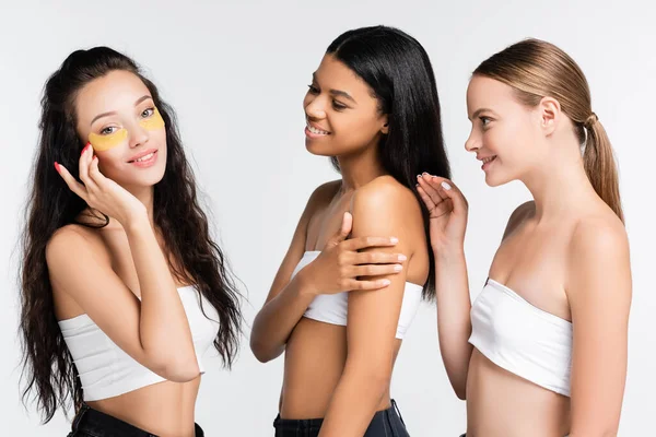 Femme brune avec des patchs d'oeil souriant et regardant la caméra près d'amis multiculturels isolés sur blanc — Photo de stock