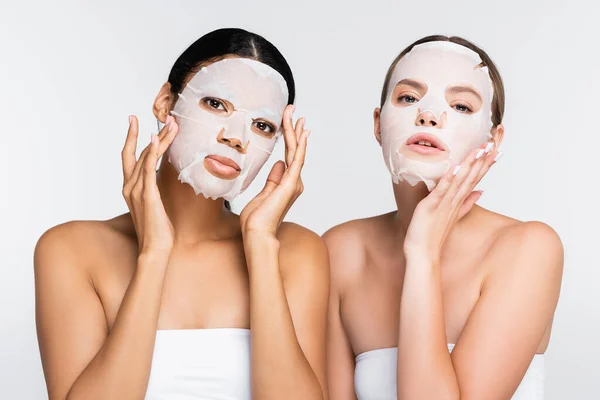 Mulheres multiétnicas jovens aplicando máscaras de folhas hidratantes isoladas em branco — Fotografia de Stock
