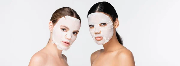 Junge interrassische Frauen in feuchtigkeitsspendenden Laken-Masken isoliert auf weiß, Banner — Stockfoto