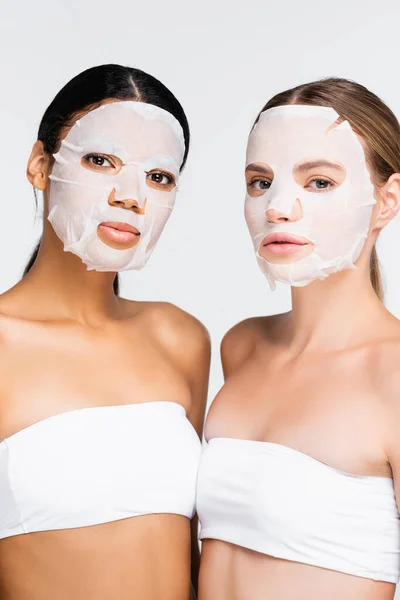 Interracial young women in moisturizing sheet masks isolated on white — Stock Photo