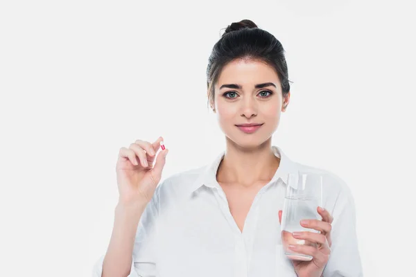 Жінка, що тримає склянку води і таблетки, дивлячись на камеру, ізольовану на білому. — стокове фото