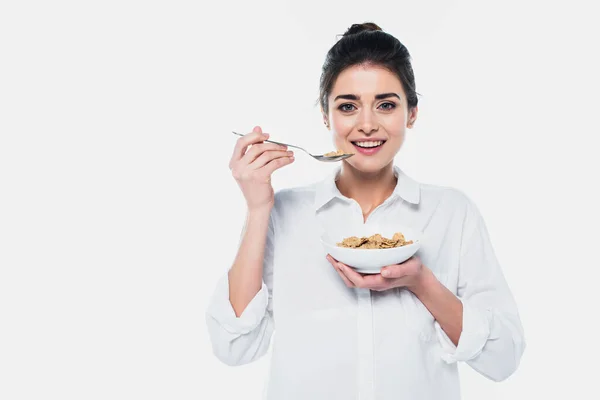 Smiling brunette woman holding spoon and bowl of cereals isolated on white — Stock Photo