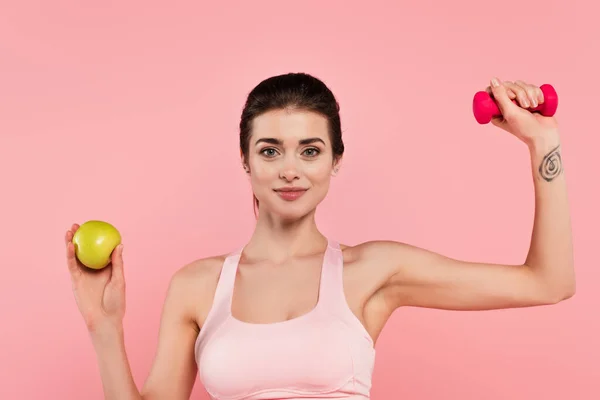 Молода спортсменка тримає гантель і яблуко ізольовано на рожевому — стокове фото