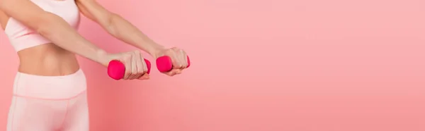 Vista recortada de mancuernas en manos de deportista en forma borrosa aislado en rosa, pancarta - foto de stock