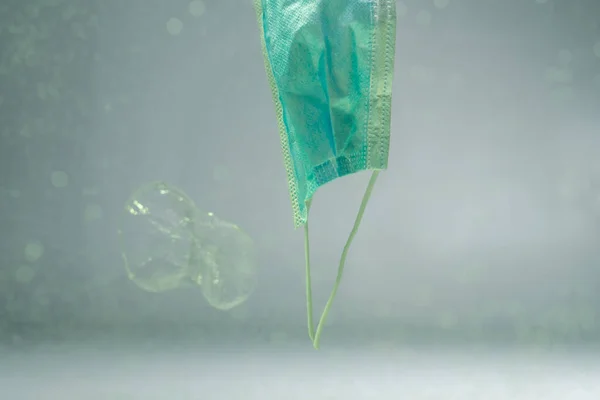 Taza de plástico y mascarilla médica usada en agua, concepto de ecología - foto de stock