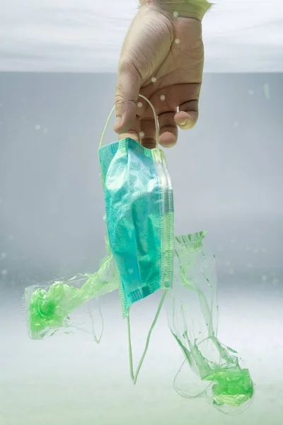 Partial view of male hand near medical mask and plastic rubbish in water, ecology concept — Stock Photo