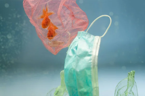 Net with goldfishes near medical mask and cellophane rubbish in water, ecology concept — Stock Photo