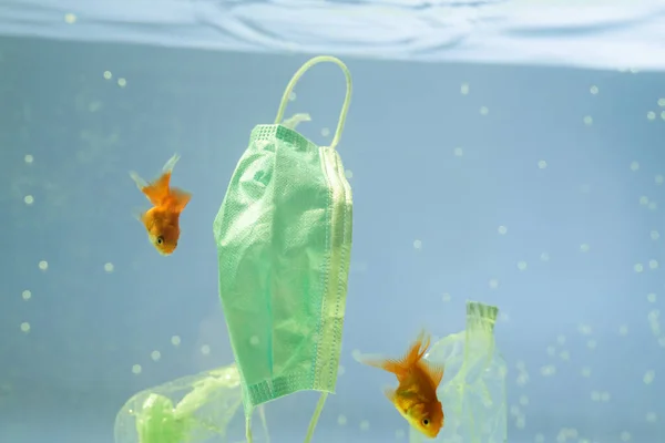 Plastic garbage and medical mask near goldfishes in water, ecology concept — Stock Photo