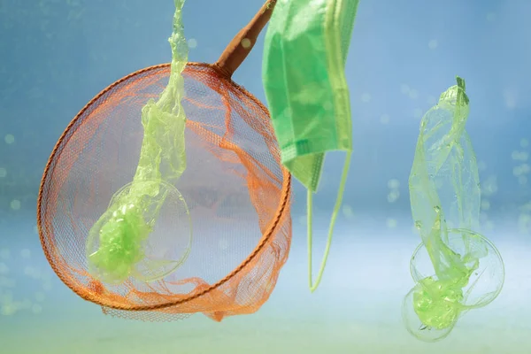 Scoop-net vicino maschera medica e sacchetti di plastica in acqua, concetto di ecologia — Foto stock