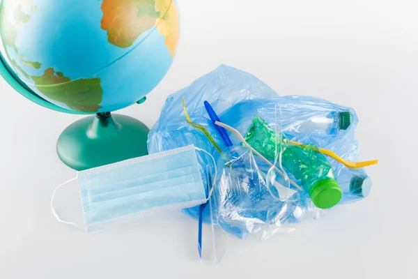 Medical mask and plastic garbage near globe on grey, ecology concept — Stock Photo
