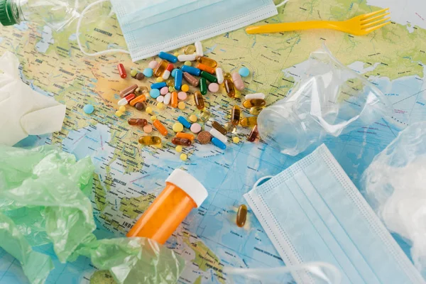 Top view of plastic garbage, medical masks and pills on map, ecology concept — Stock Photo