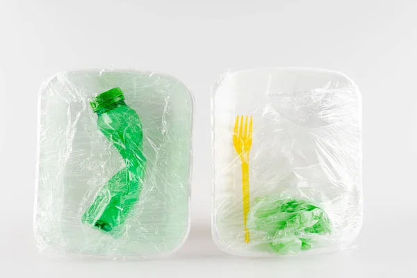 Вид сверху пластиковых пластин с бутылкой и вилкой, упакованных в полиэтилен, экологическая концепция — стоковое фото