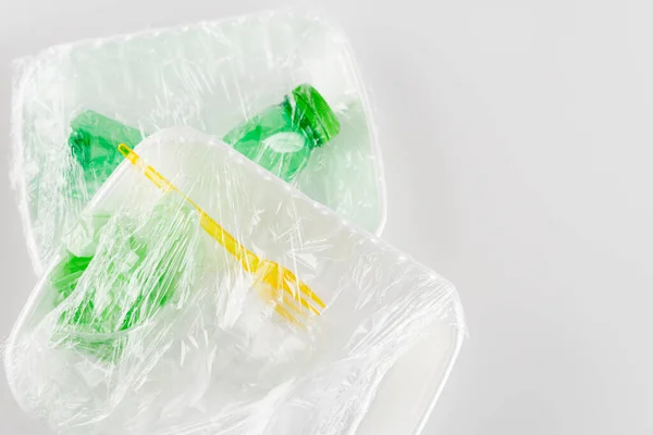 Вид сверху пластиковых пластин с вилкой и бутылкой, упакованных в целлофан, экологическая концепция — стоковое фото