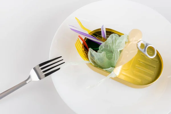 Олово с полиэтиленовым мусором на тарелке рядом с вилкой на белом, экологическая концепция — стоковое фото