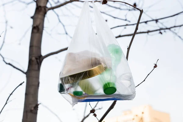 Plastic bottles and tin in cellophane bag on tree, ecology concept — Stock Photo