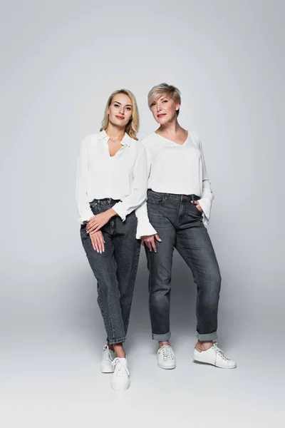 Full length view of fashionable mother and daughter looking at camera while posing on grey — Fotografia de Stock