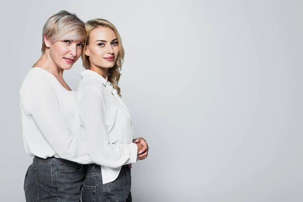 Mature woman embracing adult daughter while looking at camera isolated on grey — Foto stock