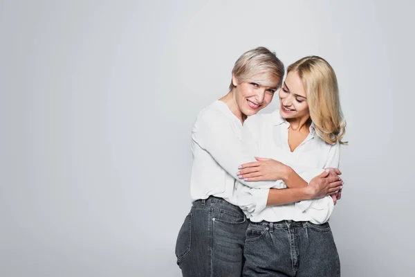 Happy mother and daughter in jeans and white blouses embracing isolated on grey — Fotografia de Stock