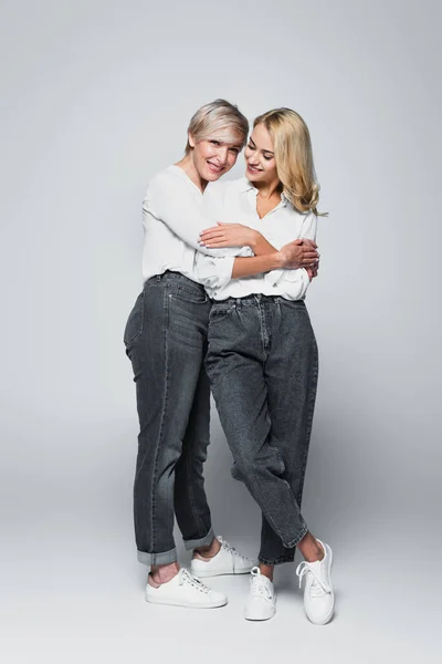 Full length view of mature woman embracing young, stylish daughter on grey — Fotografia de Stock