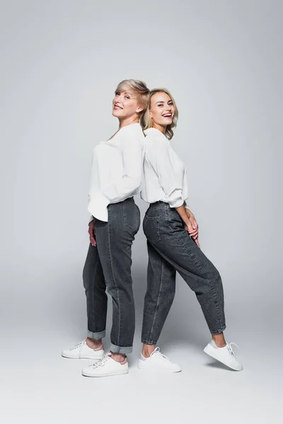 Full length view of mother and daughter in trendy clothes standing back to back on grey — Fotografia de Stock