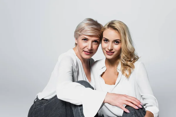 Stylish mother and daughter smiling at camera while sitting isolated on grey — Foto stock