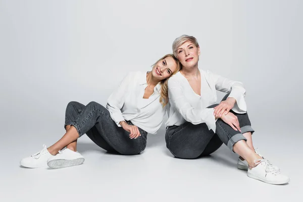 Full length view of young woman leaning on smiling mother while sitting on grey — Foto stock
