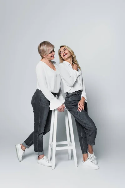 Full length view of trendy mother and daughter looking at each other near high chair on grey — Foto stock
