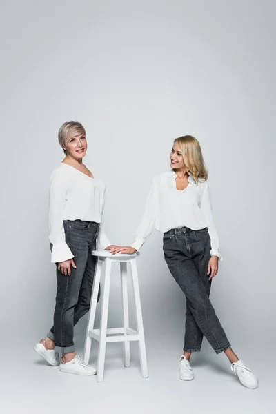 Full length view of smiling middle aged woman posing near high chair and young daughter on grey — Foto stock