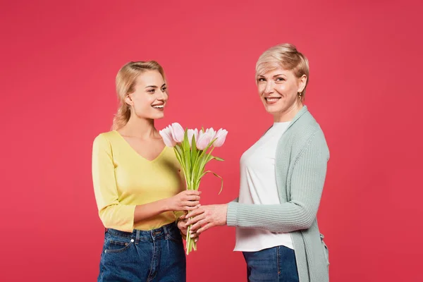 Lächelnde Frau präsentiert Tulpen der glücklichen Mutter und blickt isoliert in die Kamera auf rosa — Stockfoto