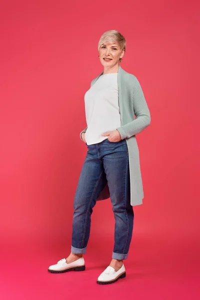 Full length view of trendy woman posing with hands in pockets of jeans on pink — Stock Photo