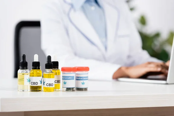 Пляшки з медичними коноплями та спартанням на столі біля лікаря на розмитому фоні. — стокове фото