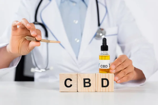 Cropped view of doctor holding bottle with cbd and joint near wooden cubes — Stock Photo