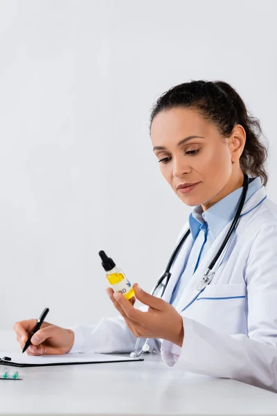 Afro-américain médecin écrivant prescription et tenant bouteille cbd — Photo de stock