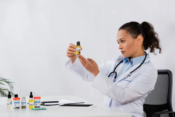 Афроамериканський лікар тримає пляшку КДБ біля ліків і цифровий планшет на столі — стокове фото