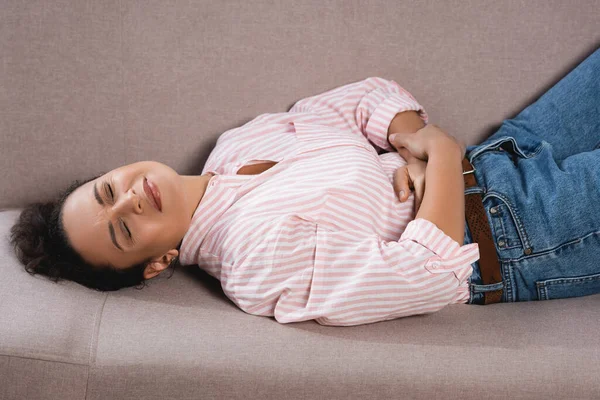 Afro-americana que sofre de dor de estômago enquanto deitado no sofá — Fotografia de Stock