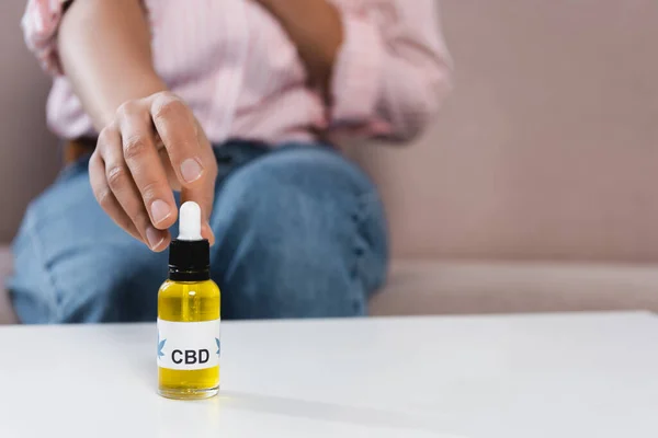 Partial view of blurred african american woman reaching bottle with cbd letting on table — Stock Photo