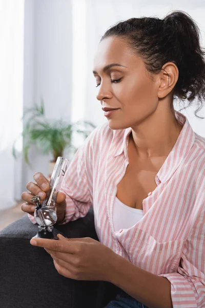 Mujer afroamericana sosteniendo pipa de vidrio con cannabis medicinal seco - foto de stock