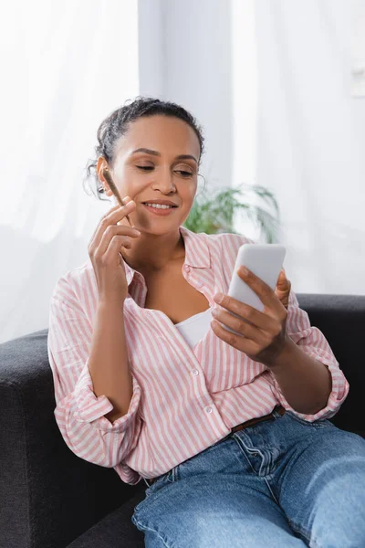 Happy african american woman holding rolled joint with medical cannabis and using smartphone — Stock Photo