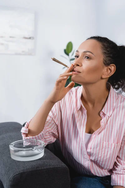 Afrikanische Amerikanerin raucht RollJoint mit medizinischem Cannabis in der Nähe von Aschenbecher — Stockfoto