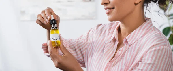 Cropped view of happy african american woman holding bottle with cbd lettering and pipette, banner — Stock Photo