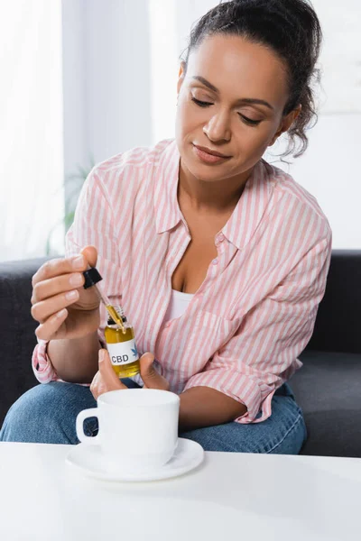 Афроамериканська жінка тримає піпетку і пляшку з КДБ, що розкладається біля чашки на столі — стокове фото