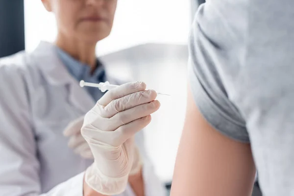 Vista recortada de la jeringa en la mano del médico cerca del paciente en primer plano borroso - foto de stock